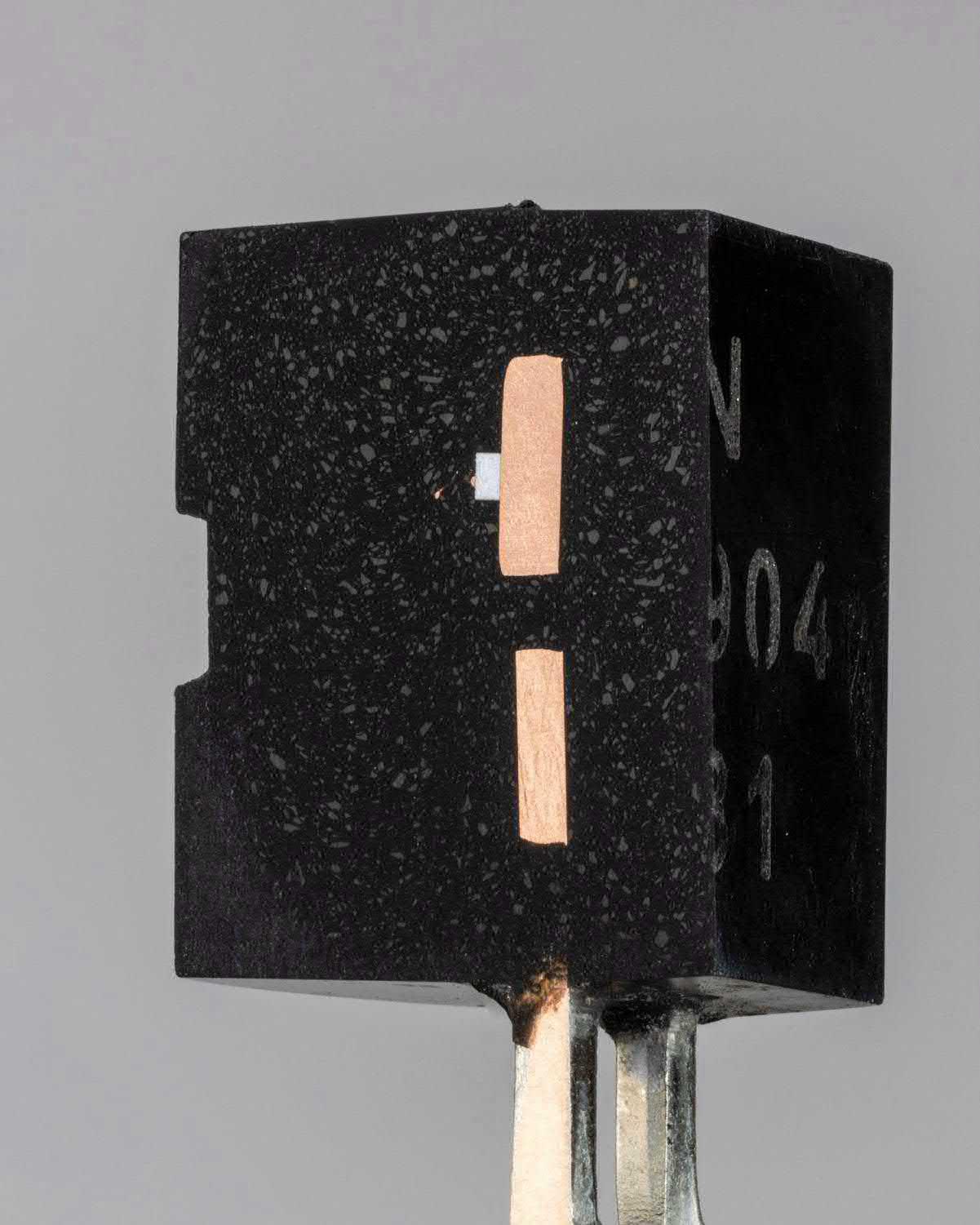 Neben dem Siliziumchip im Inneren des Transistors ist einer der beiden goldenen Bond-Drähte sichtbar.